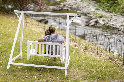 Rückansicht des lächelnden Sitzens auf einer Schaukel im Garten, lizenzfreies Stockfoto