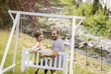 Porträt eines lächelnden Paares, das auf einer Schaukel im Garten sitzt - MJFKF00070