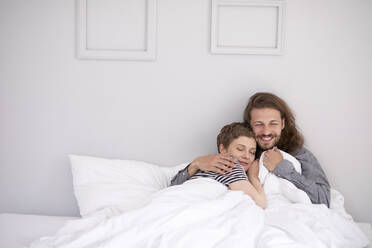 Glückliches junges Paar, das zu Hause im Bett kuschelt - MJFKF00073