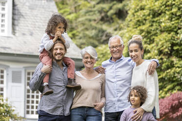 Eine glückliche Großfamilie steht im Garten ihres Hauses - MJFKF00076