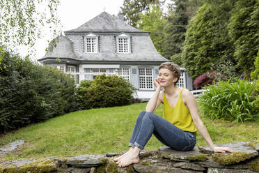 Entspannte Frau sitzt auf einer Mauer im Garten - MJFKF00083