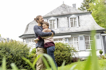 Happy young couple hugging in garden of their home - MJFKF00087