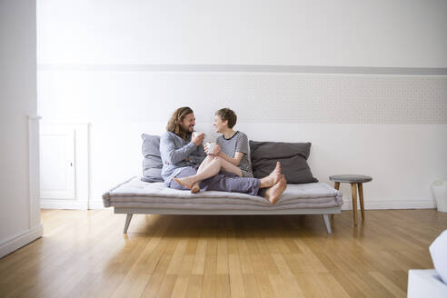 Glückliches junges Paar im Pyjama auf der Couch zu Hause - MJFKF00091