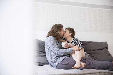 Junges Paar im Pyjama küsst sich auf der Couch zu Hause - MJFKF00093