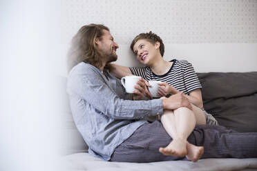 Glückliches junges Paar im Pyjama auf der Couch zu Hause - MJFKF00094
