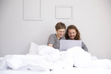 Junges Paar mit Laptop im Bett zu Hause - MJFKF00096