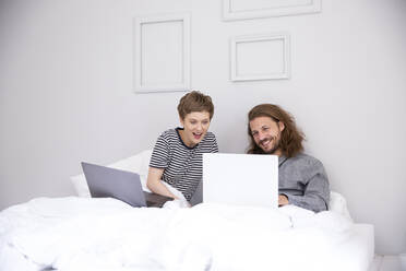 Junges Paar mit Laptops im Bett zu Hause - MJFKF00098