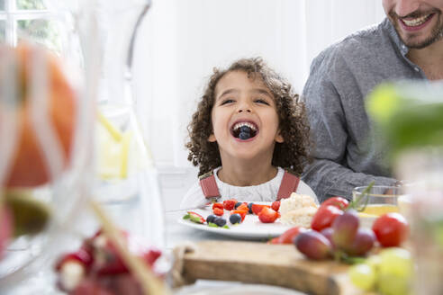 Verspielter Junge mit seinem Vater, der am Tisch Blaubeeren isst - MJFKF00115