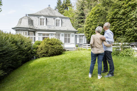 Rear view of senior couple standing in garden of their home stock photo