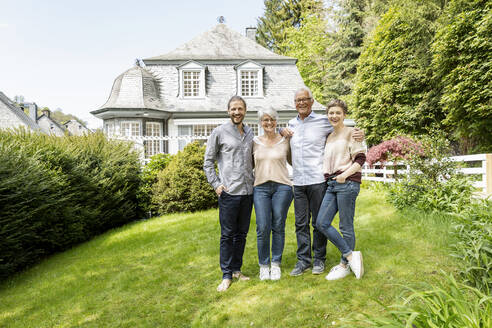 Happy senior couple with adult children standing in garden of their home - MJFKF00126