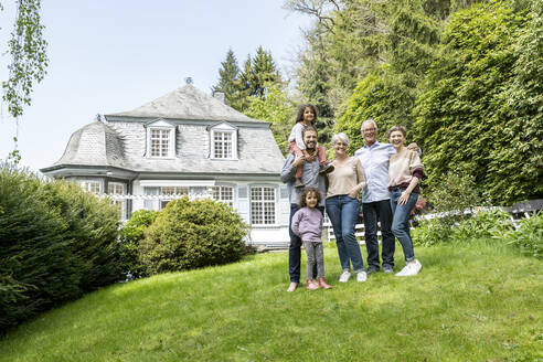 Happy extended family standing in garden of their home - MJFKF00129