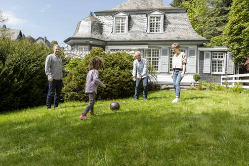 Glückliche Großfamilie beim Fußballspielen im Garten - MJFKF00132