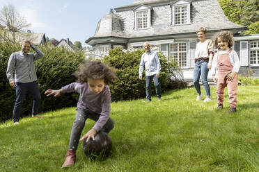 Glückliche Großfamilie beim Fußballspielen im Garten - MJFKF00134