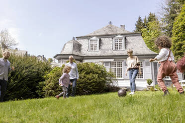 Happy extended family playing football in garden - MJFKF00135