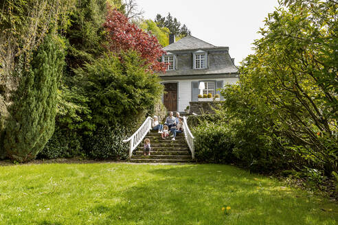 Großfamilie sitzt auf einer Treppe im Garten ihres Hauses - MJFKF00137