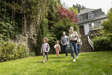 Glückliche Großfamilie bei einem Spaziergang im Garten ihres Hauses - MJFKF00138