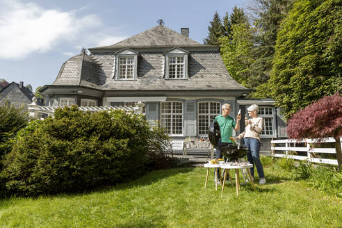 Glückliches älteres Paar beim Grillen im Garten ihres Hauses - MJFKF00140