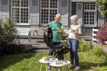 Glückliches älteres Paar beim Grillen im Garten ihres Hauses - MJFKF00141