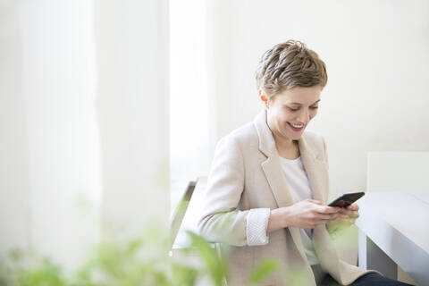 Lächelnde Frau, die zu Hause ein Mobiltelefon benutzt, lizenzfreies Stockfoto