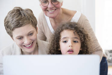 Lächelnde Großmutter, Mutter und Sohn benutzen einen Laptop zu Hause - MJFKF00147