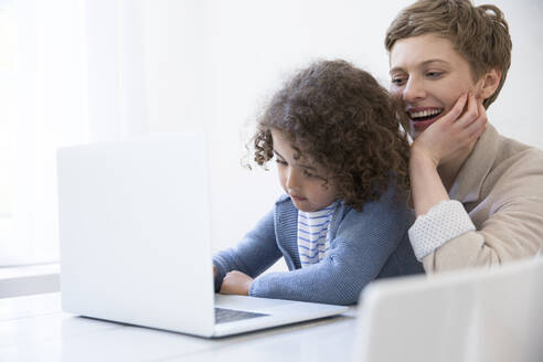 Lächelnde Mutter und Sohn verwenden Laptop zu Hause - MJFKF00148
