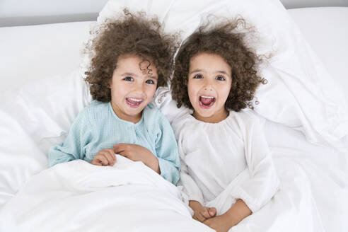 Porträt von zwei glücklichen Zwillingsbrüdern, die im Bett liegen - MJFKF00162