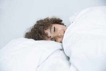 Porträt eines im Bett liegenden Jungen mit lockigem Haar - MJFKF00166