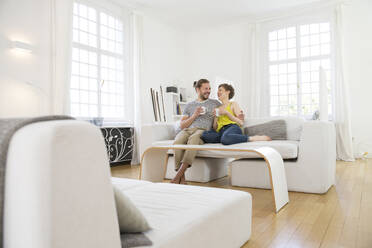 Glückliches junges Paar sitzt zu Hause auf der Couch - MJFKF00170