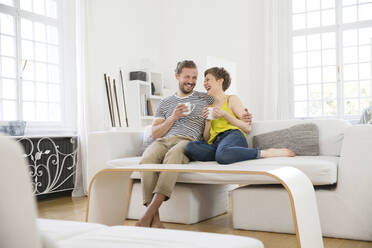 Lachendes junges Paar sitzt zu Hause auf der Couch - MJFKF00171