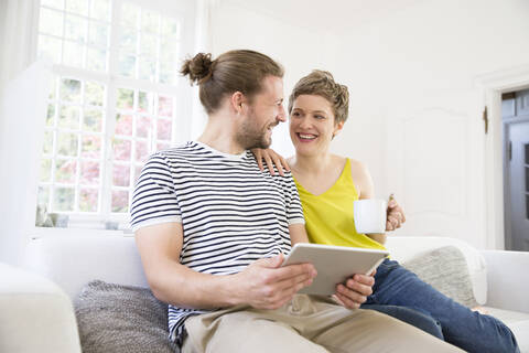 Glückliches junges Paar benutzt Tablet auf der Couch zu Hause, lizenzfreies Stockfoto