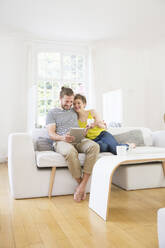 Happy young couple using tablet on couch at home - MJFKF00173
