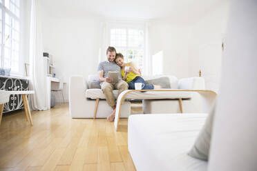 Glückliches junges Paar benutzt Tablet auf der Couch zu Hause - MJFKF00174