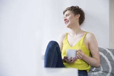 Smiling woman with cup of coffee at home - MJFKF00182