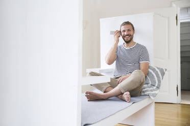 Lächelnder junger Mann, der zu Hause sein Smartphone benutzt - MJFKF00183