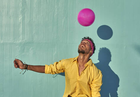 Young black man playing with a pink ball in front of a blue wall - VEGF00674