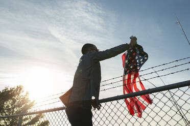 Junger Mann entfernt US-amerikanische Flagge vom Maschendrahtzaun - JPTF00321