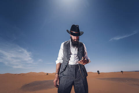 Mann mit Bart und Hut in den Dünen der Wüste von Marokko bei der Zeitkontrolle, lizenzfreies Stockfoto