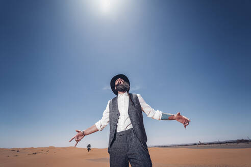 Man with a beard and hat screaming in the dunes of the desert of Morocco - OCMF00720