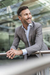 Smiling businessman in the city leaning on railing - DIGF08391