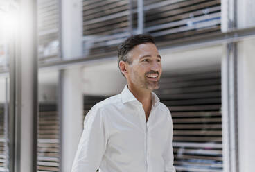 Smiling businessman at a car park wearing white shirt - DIGF08394