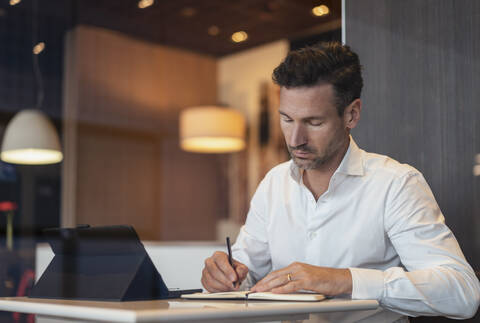 Geschäftsmann mit Tablet in einem Café macht sich Notizen, lizenzfreies Stockfoto