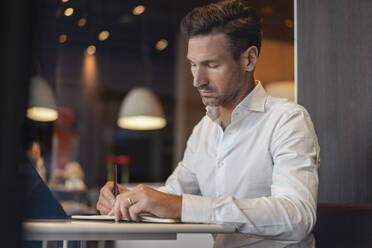 Businessman with tablet in a cafe taking notes - DIGF08397