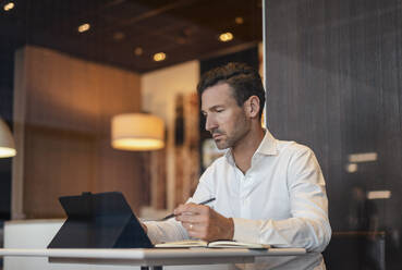 Businessman using tablet and taking notes in a cafe - DIGF08398