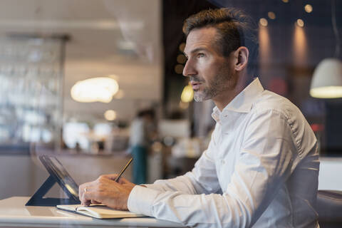 Geschäftsmann mit Tablet in einem Café macht sich Notizen, lizenzfreies Stockfoto