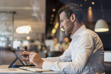 Businessman using tablet and taking notes in a cafe - DIGF08400