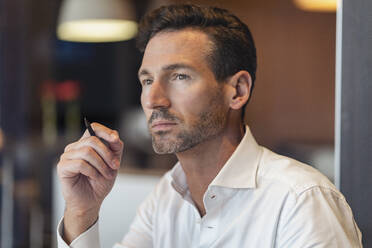 Portrait of thoughtful businessman holding pen - DIGF08403