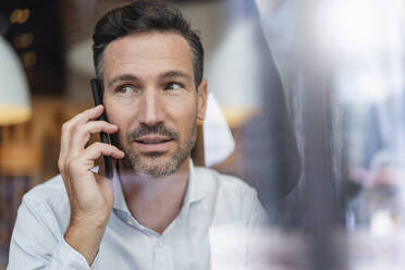 Portrait of businessman on the phone behind windowpane in a cafe - DIGF08408