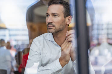 Portrait of businessman behind windowpane in a cafe - DIGF08409