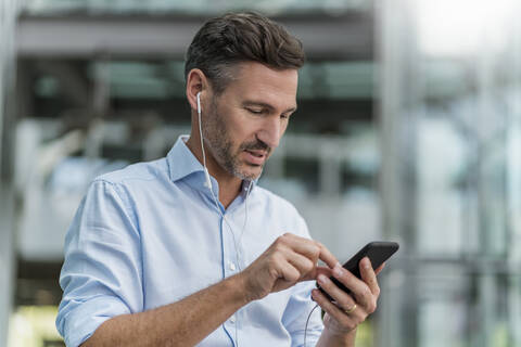 Geschäftsmann mit Kopfhörer und Mobiltelefon in der Stadt, lizenzfreies Stockfoto