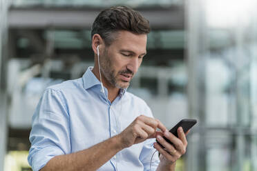 Businessman with earphones and cell phone in the city - DIGF08436